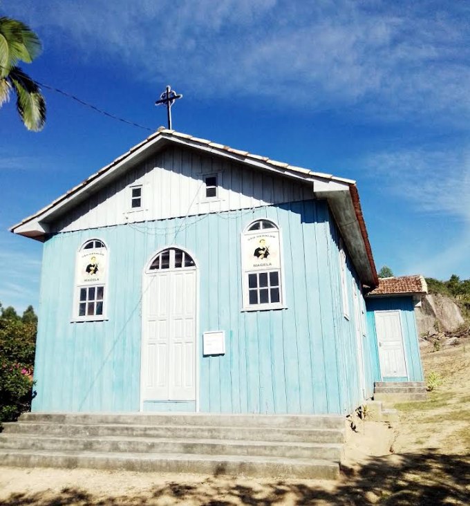 A capela em ângulo, com a palmeira à esquerda e a escadaria de concreto na entrada.